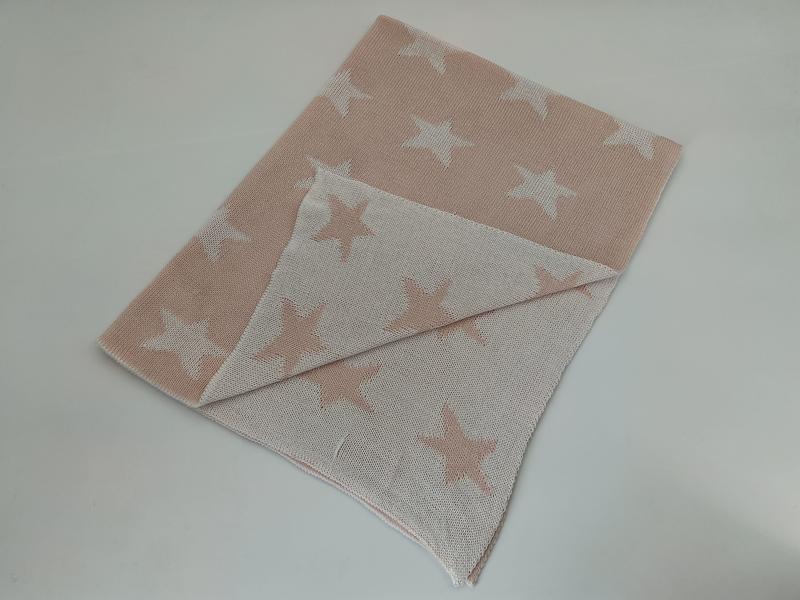 Coperta in maglia di cotone reversibile rosa blush e bianca con motivo a croce, presentata piegata per mostrare il design bicolore su entrambi i lati. Texture morbida a intreccio, stile nordico minimal, ideale come accessorio decorativo per divano o