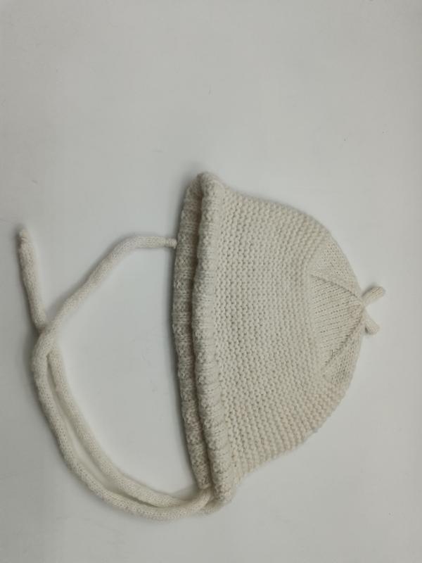 Cuffietta neonato color crema lavorata a maglia a mano con lacci sottogola, realizzata a punto legaccio in morbida lana avorio. Accessorio artigianale per bebè, presentata su sfondo bianco. Ideale per boutique ingrosso abbigliamento neonato e corredi