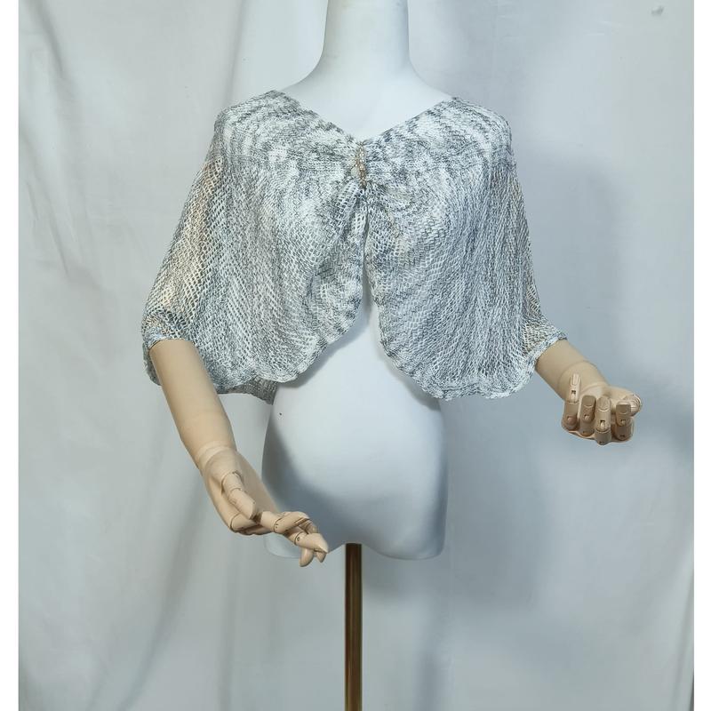 Capelet in mesh traslucido con stampa snakeskin grigio-bianca e chiusura con spilla decorativa, indossata su manichino bianco. Mantellina elegante in tessuto a rete semitrasparente con motivo pelle di serpente, ideale per look moda donna raffinati e