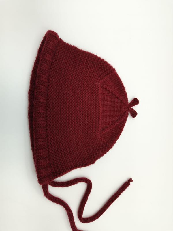 Cuffietta neonato fatta a mano color rosso cremisi con bordo a balza, texture punto garter e laccetti sottogola. Cappellino invernale lavorato a maglia, ideale per neonati, in morbida lana artigianale. Accessorio bambino elegante e caldo, perfetto co