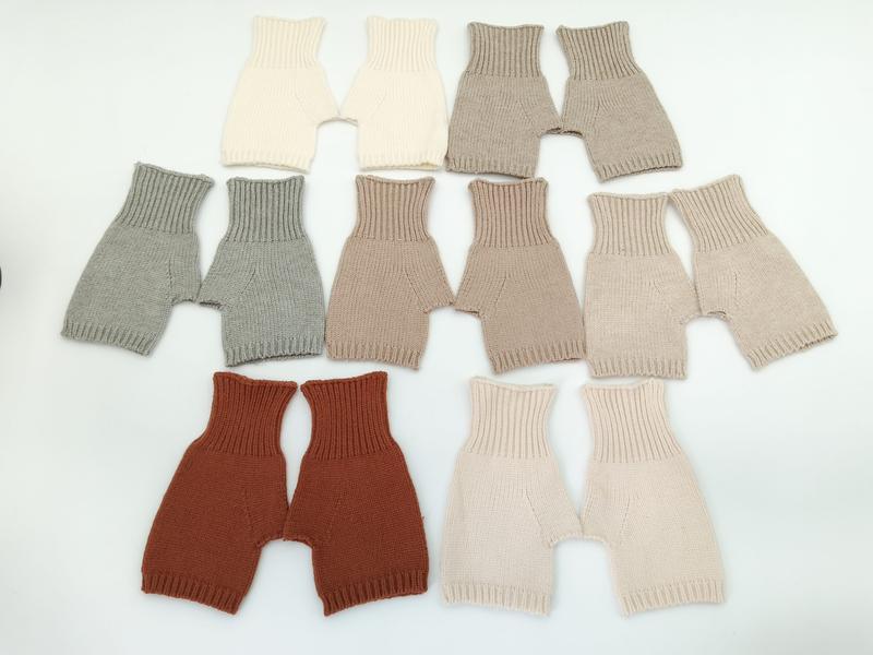 Set di 7 paio di bloomers shorts neonato lavorati a maglia artigianalmente, disposti in piano. Colori neutri naturali: crema, grigio, taupe, beige, ruggine, cipria e sabbia. Pantaloncini corti in maglia per bebè, ideali per layering, in tonalità terr