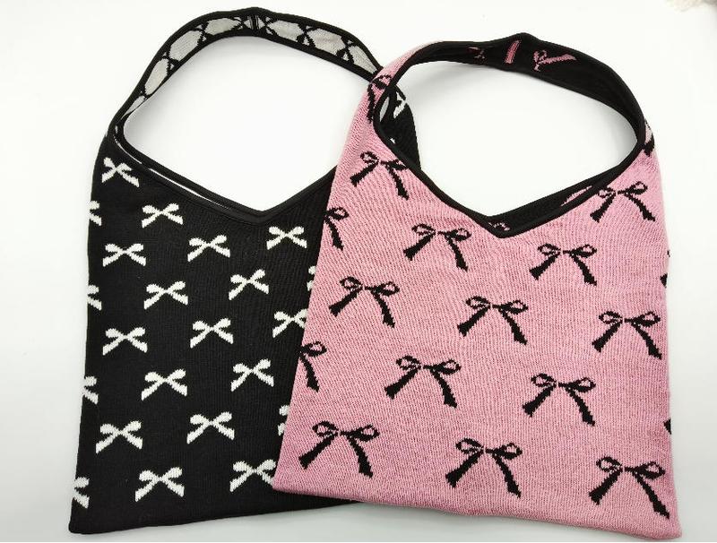 Due borse hobo in maglia con pattern di fiocchi all-over: una nera con fiocchi bianchi e una rosa con fiocchi neri. Stile boho-chic, materiale knit morbido e strutturato, manici a spalla. Set di borse donna all'ingrosso ideale per boutique e rivendit