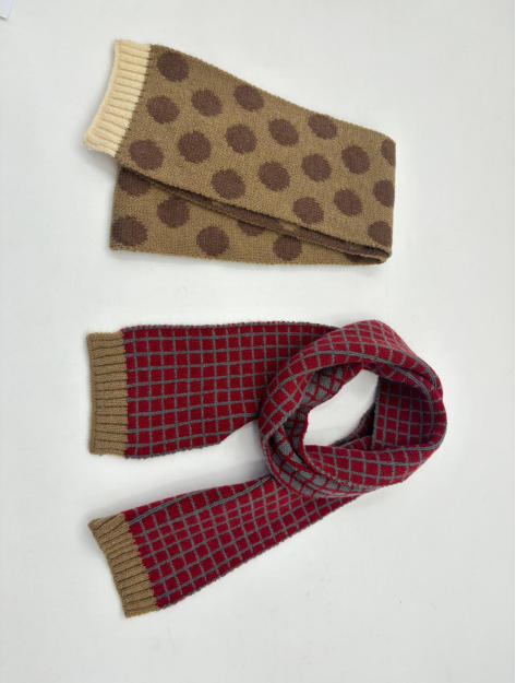Due sciarpe in maglia disposte in piano: una color cuoio con pois marroni e bordi a coste color crema, l'altra rossa con motivo a griglia grigia. Accessori invernali all'ingrosso in tricot, ideali per look casual e moderni. - private label wholesale