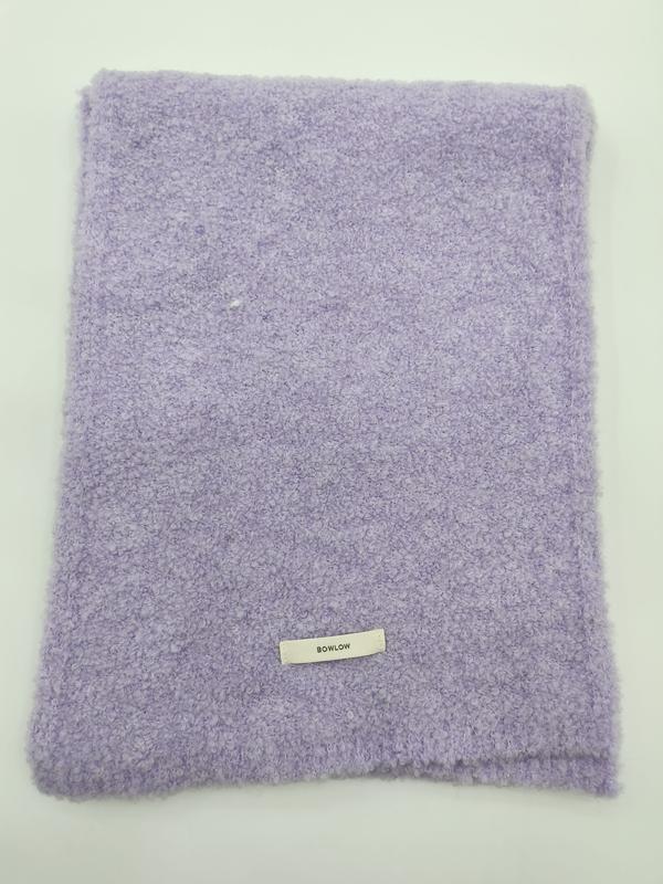 Coperta plaid lavanda in morbido tessuto bouclé con texture arricciata, piegata con etichetta su sfondo bianco. Accessorio moda all'ingrosso in delicato color lilla, ideale come throw blanket dal look elegante e contemporaneo. Perfetta per arredament