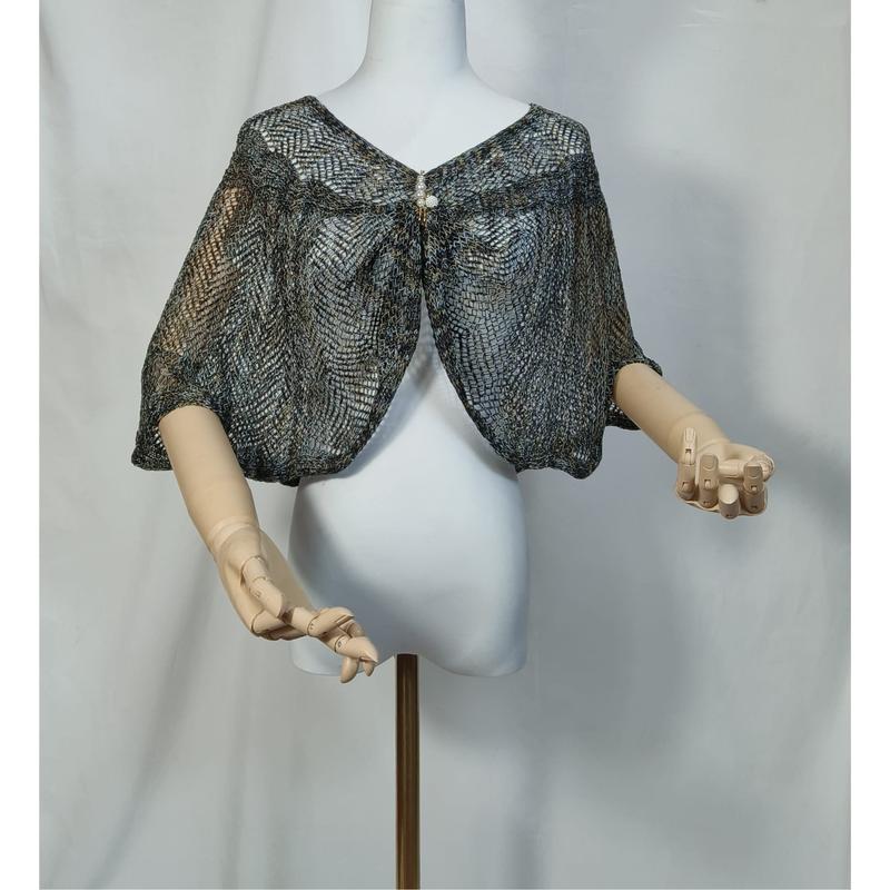 Capelet shrug in maglia di pizzo metallizzato blu grigio con spilla di perle, indossato su manichino bianco con mani in legno. Accessorio fashion all'ingrosso in filato luccicante, stile elegante e romantico, chiusura centrale con fermaglio decorativ