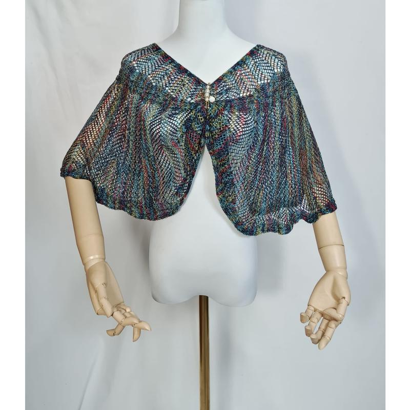 Capet in maglia a rete multicolore con intreccio aperto nei toni teal, rosso e oro, esposta su manichino. Il mantellino presenta una chiusura con spilla decorativa di perle, ideale come accessorio moda donna all'ingrosso. Tessuto leggero e raffinato