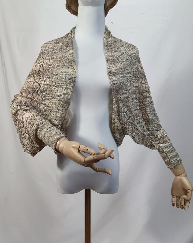 Bolero shrug cardigan a maglia traforata in pizzo open-front, color beige grigio mélange, esposto su manichino in legno articolato. Cardigan donna all'ingrosso in lavoro a maglia aperto sul davanti, ideale come capospalla leggero in stile boho. Dispo