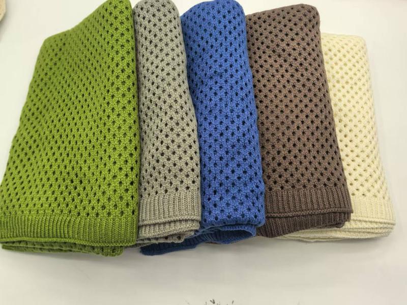 Cinque coperte in maglia di cotone open weave all'ingrosso, pieghettate e impilate, disponibili in cinque colori: verde, grigio, blu, marrone e crema. Tessuto leggero e traspirante con intreccio aperto, ideali come throw blanket da divano o letto. St