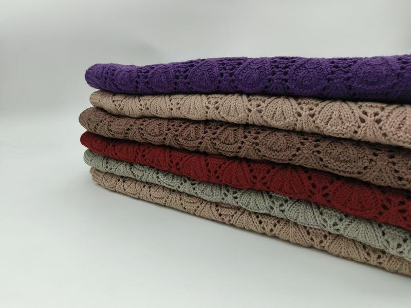 Pila di sei coperte plaid all'uncinetto traforato in maglia, ripiegate e impilate, disponibili in colori assortiti: viola, beige, talpa, rosso, verde salvia e cuoio. Coperte decorative in stile lavorazione aperta, ideali come throw da divano, disponi