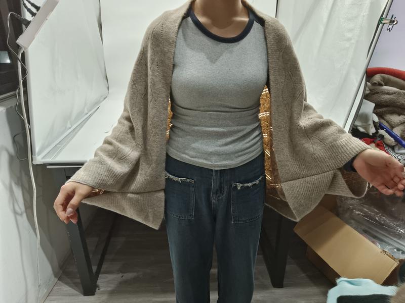 Cardigan oversize beige in maglia a maglia grossa, modello aperto sul davanti con maniche ampie. Indossato su top grigio a coste e jeans denim, perfetto look casual-chic da donna. Capo all'ingrosso ideale per la stagione autunno-inverno. - B2B direct
