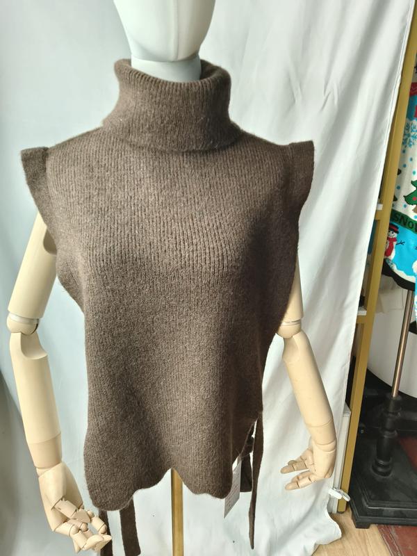 Gilet maglione senza maniche color tortora in maglia a collo alto con lacci laterali, esposto su manichino. Capo in maglia turtleneck dal design elegante e contemporaneo, con dettagli tie laterali che valorizzano la silhouette. Ideale per look layeri
